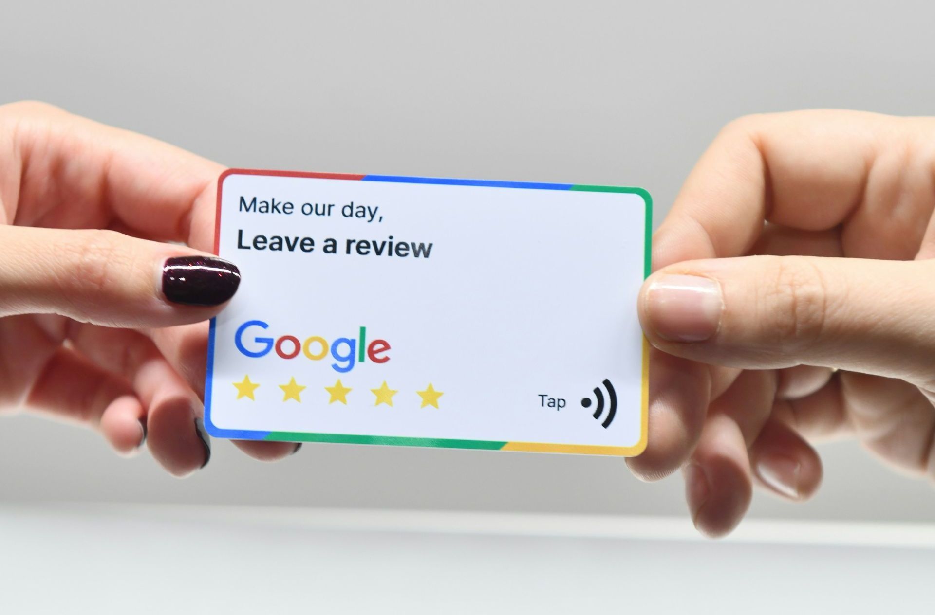 A person is holding a google review card in front of an apple laptop.