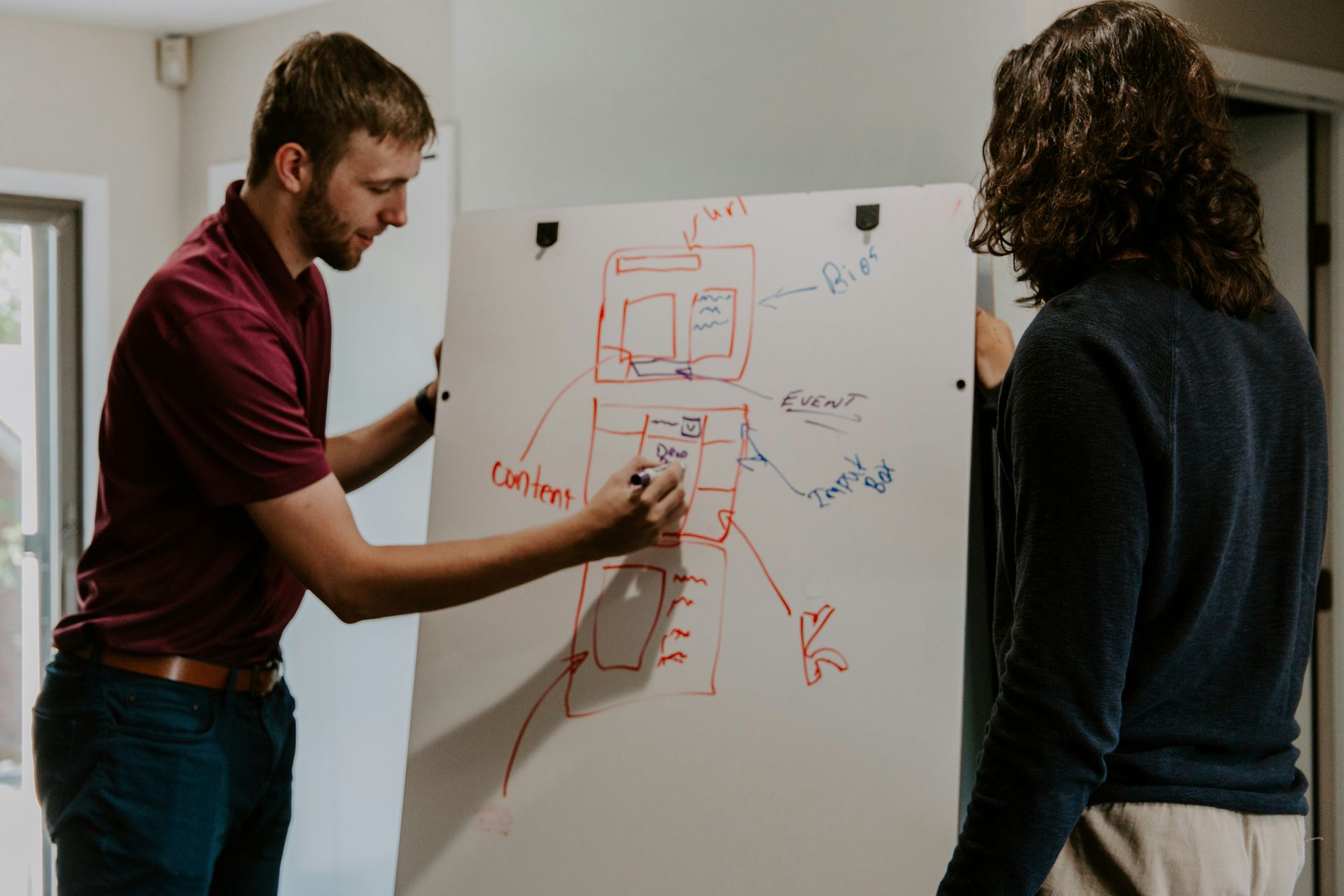 A man and a woman are standing in front of a whiteboard.