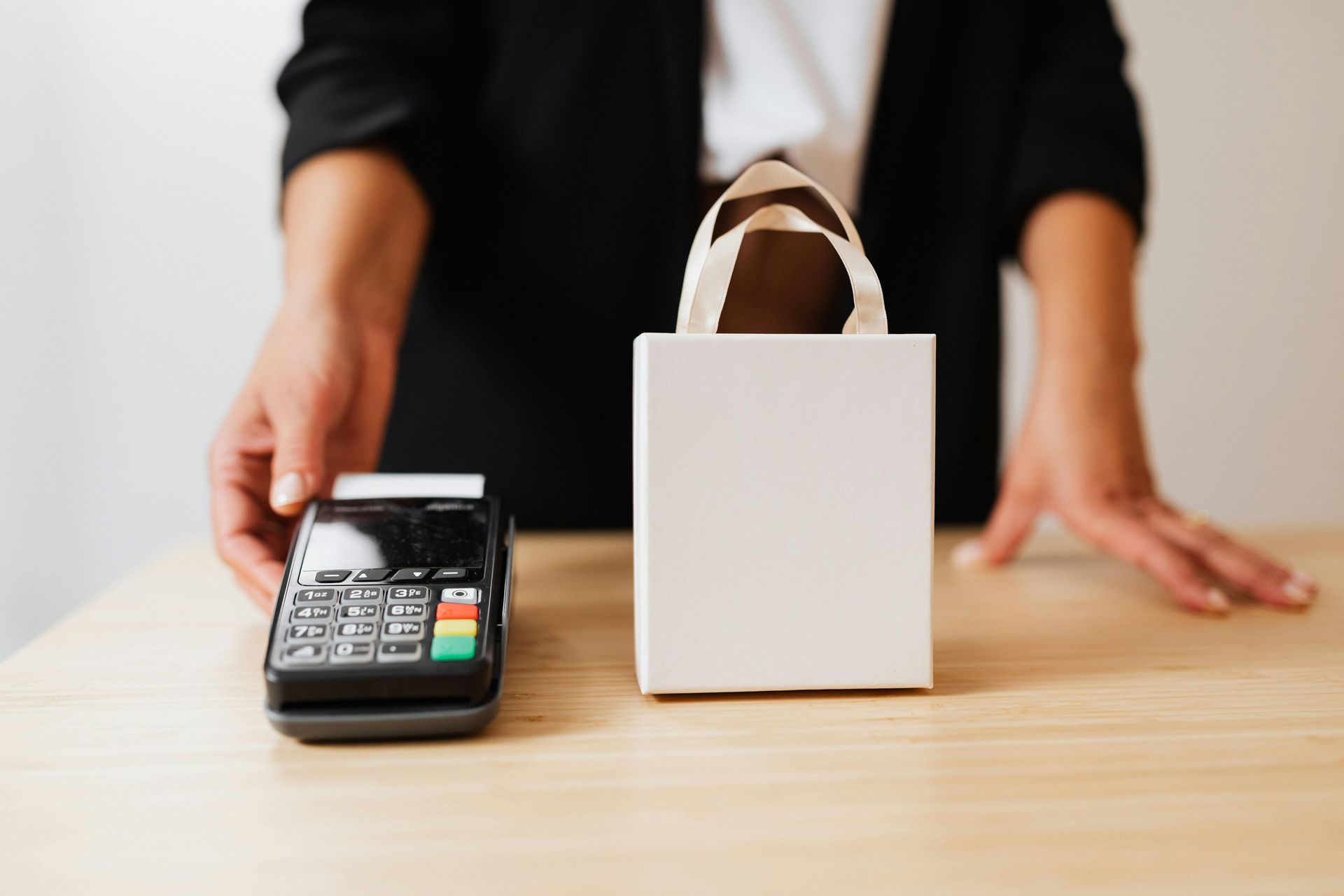 Person at counter with payment terminal and blank white shopping bag.