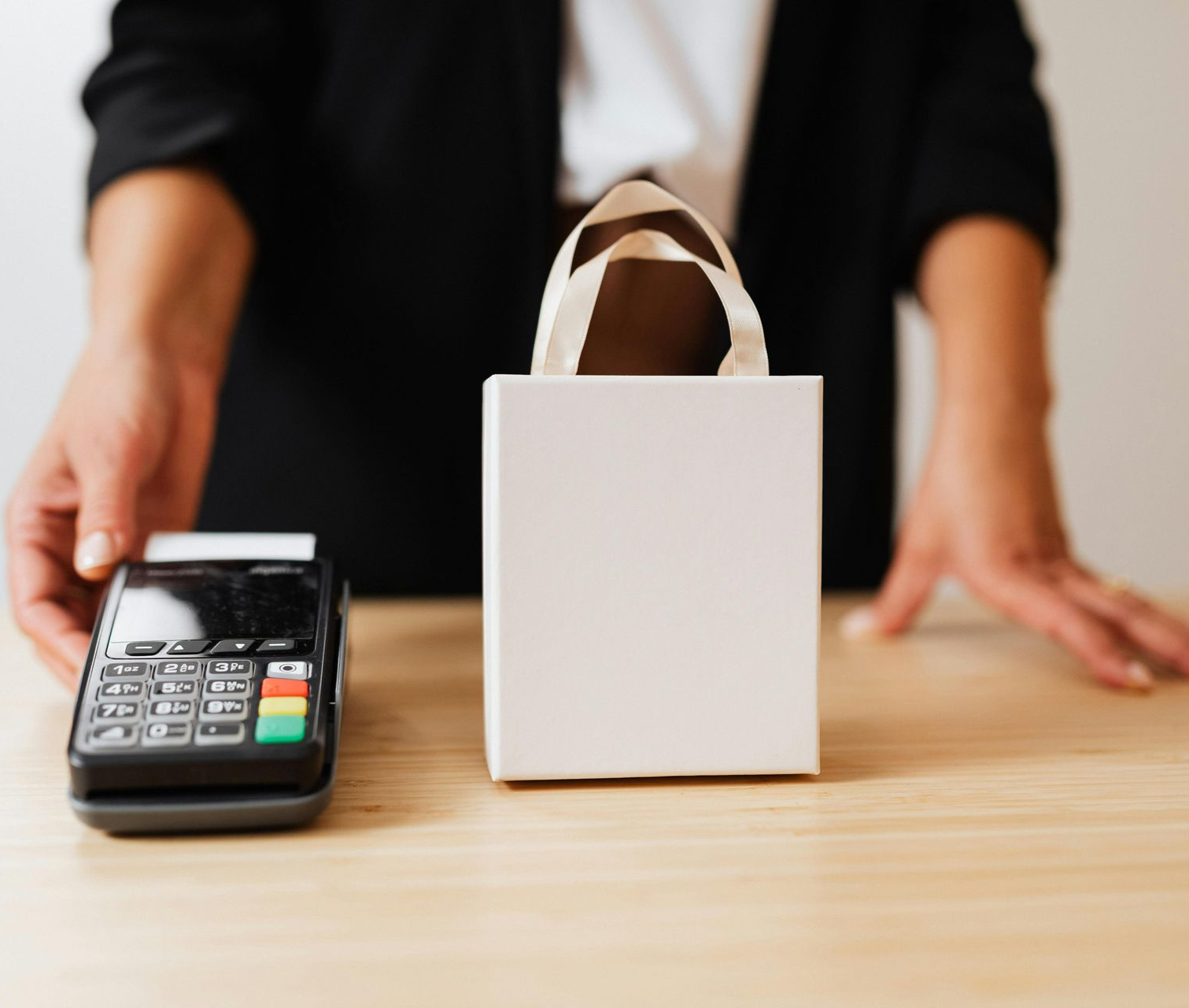 Person at a checkout counter with a card reader and a shopping bag on the table