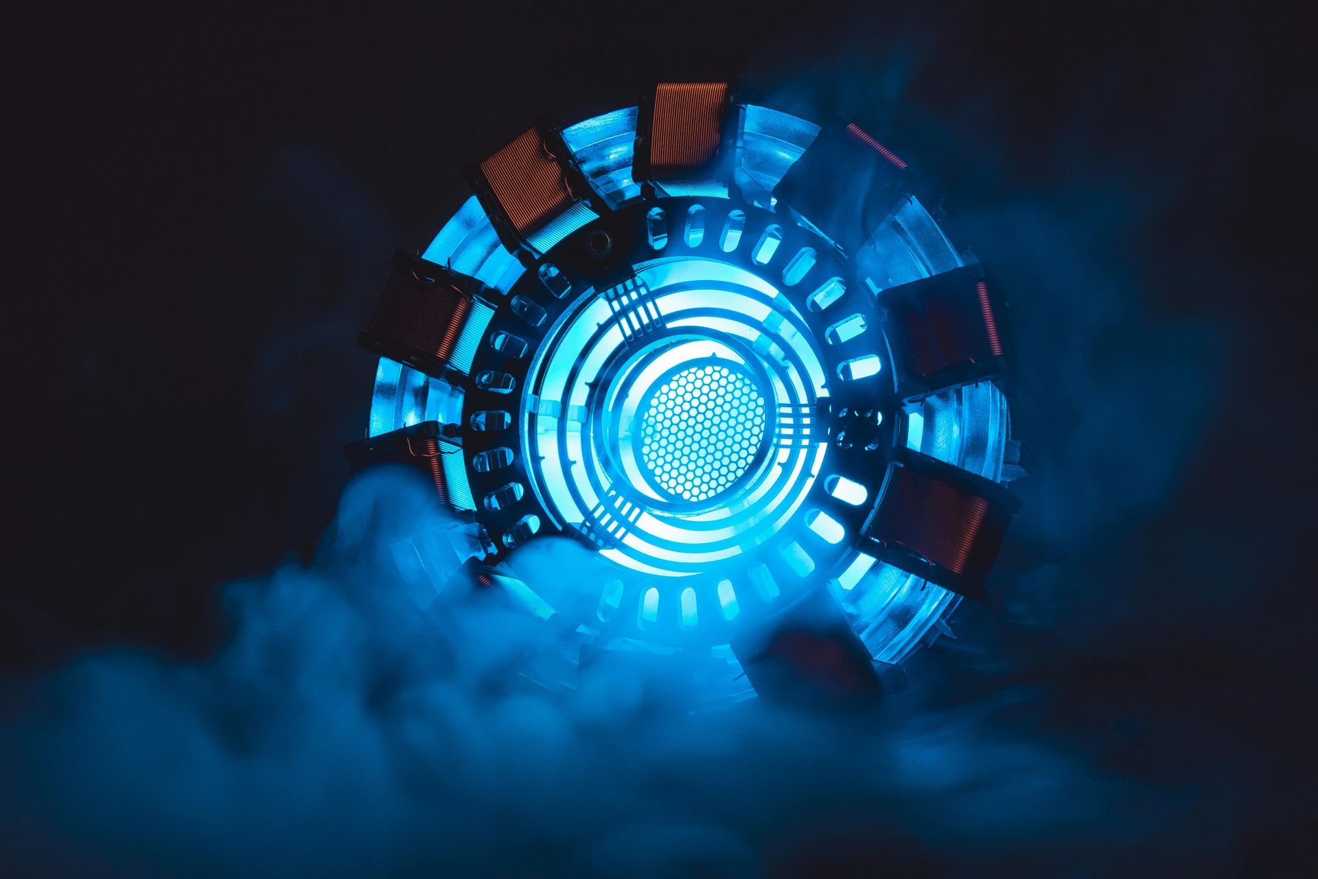 Glowing blue arc reactor from Iron Man, emitting blue vapor on a dark background.