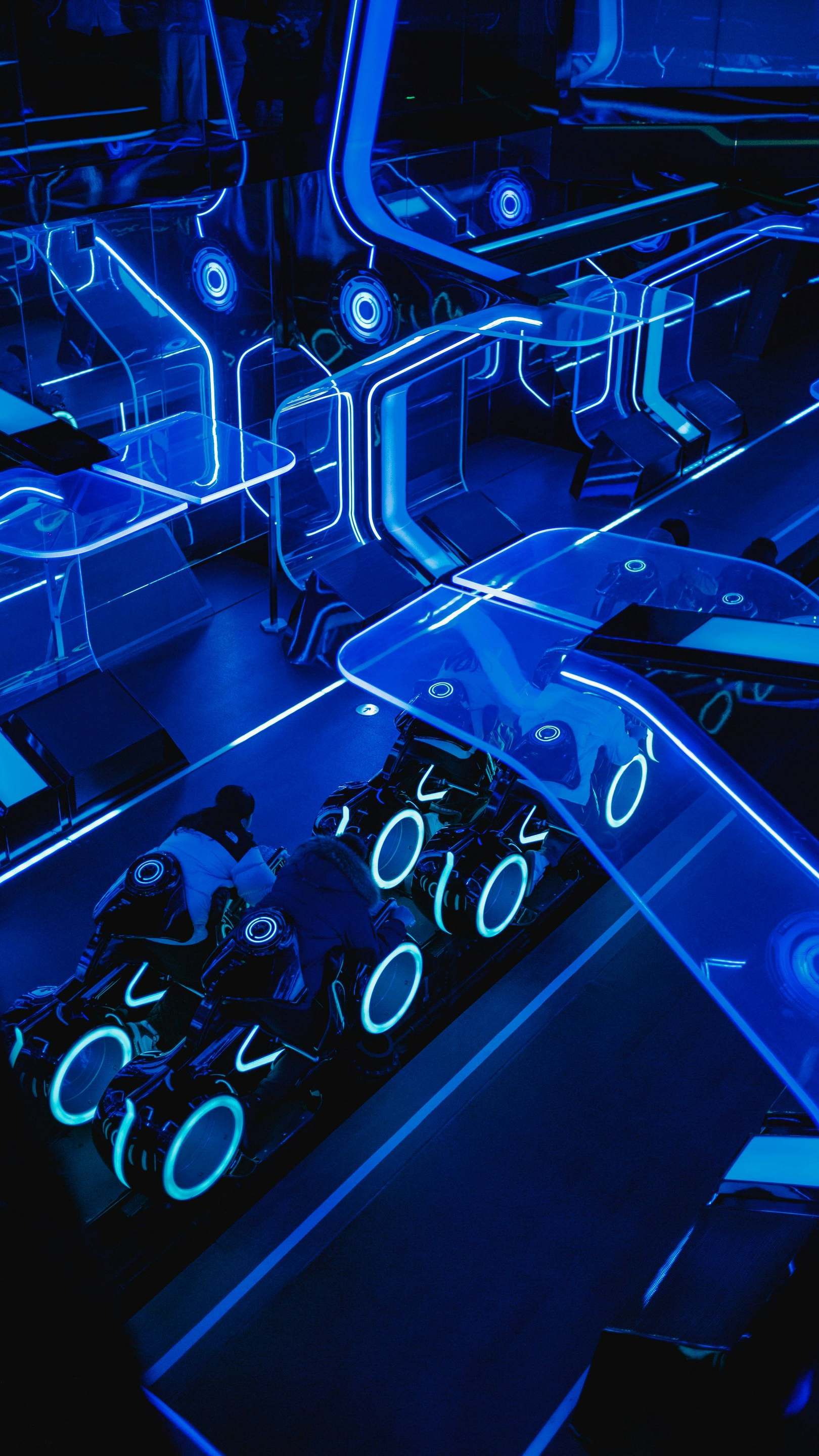 Neon blue TRON Lightcycle coaster cars on futuristic track.