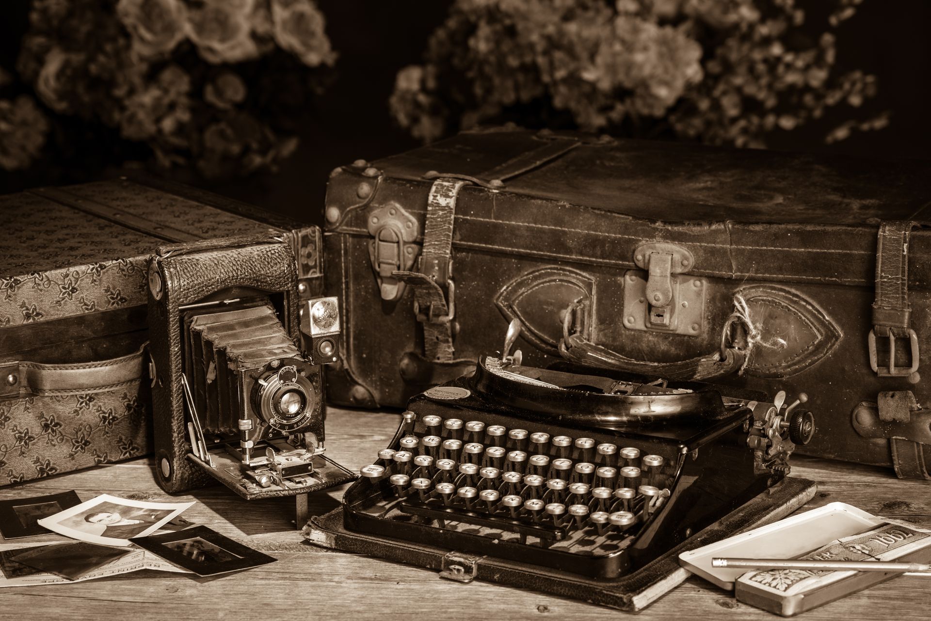 An old typewriter is sitting on a wooden table next to a suitcase.