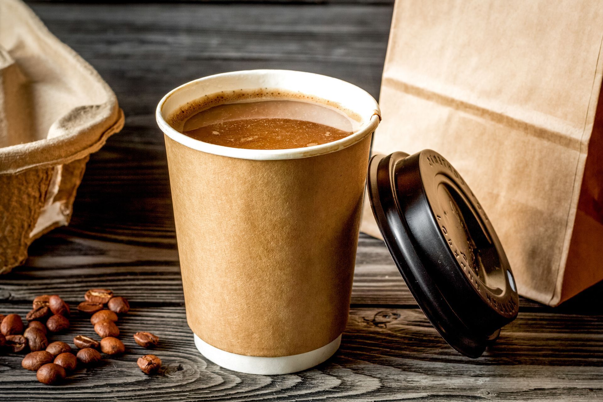 A cup of coffee is sitting on a wooden table next to a paper bag.
