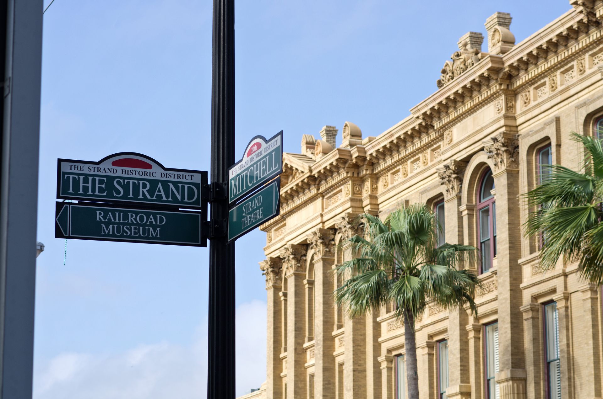 A street sign for the strand railroad museum is hanging on a pole in front of a large building.