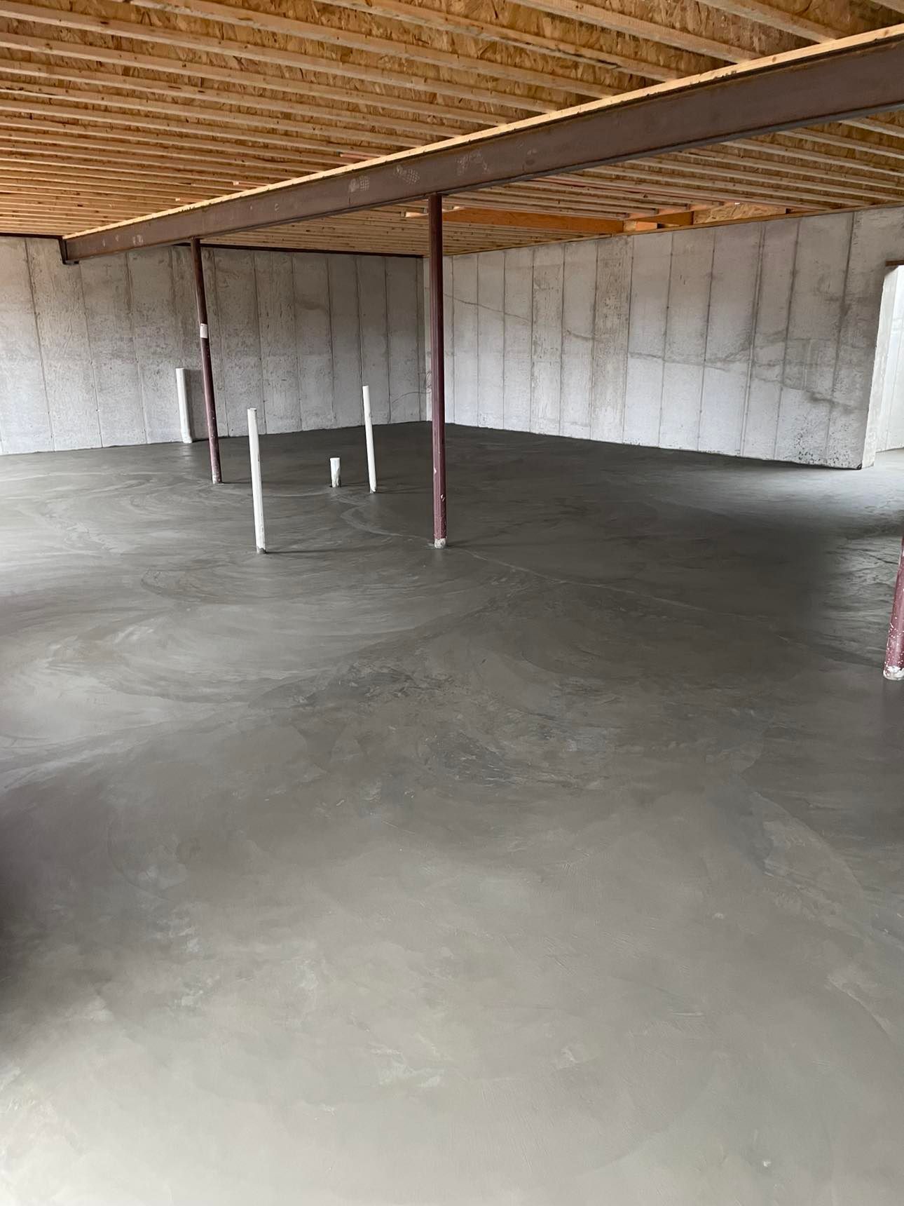 A concrete floor in a basement with a wooden ceiling.