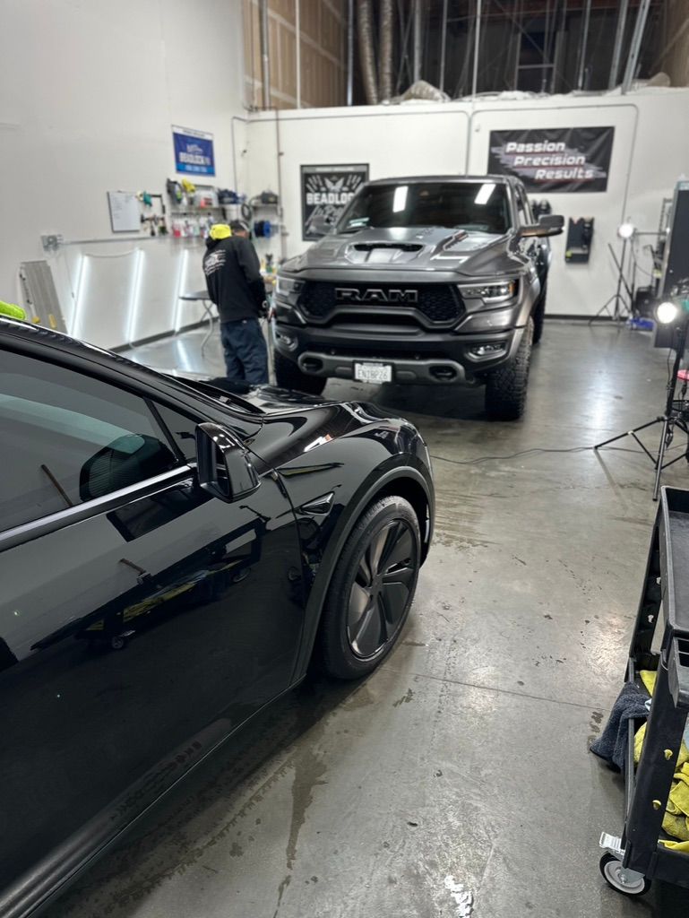 A garage featuring a black truck in the foreground and a gray RAM truck in the background, with a worker standing nearby.