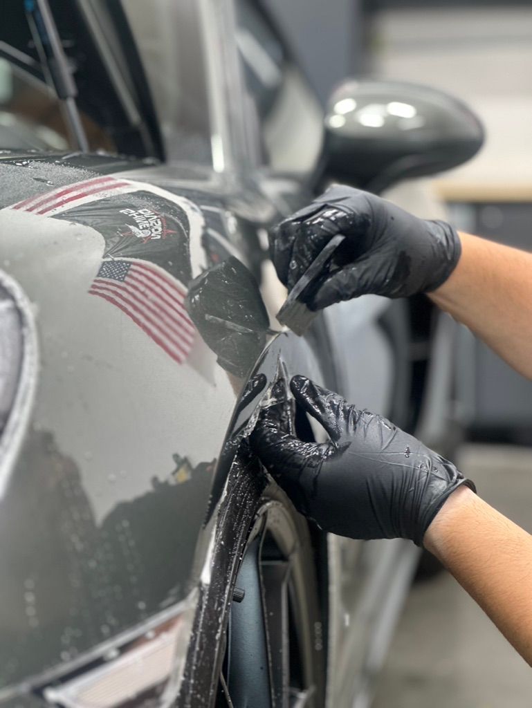 Hands in black gloves applying protective film to a gray car door.
