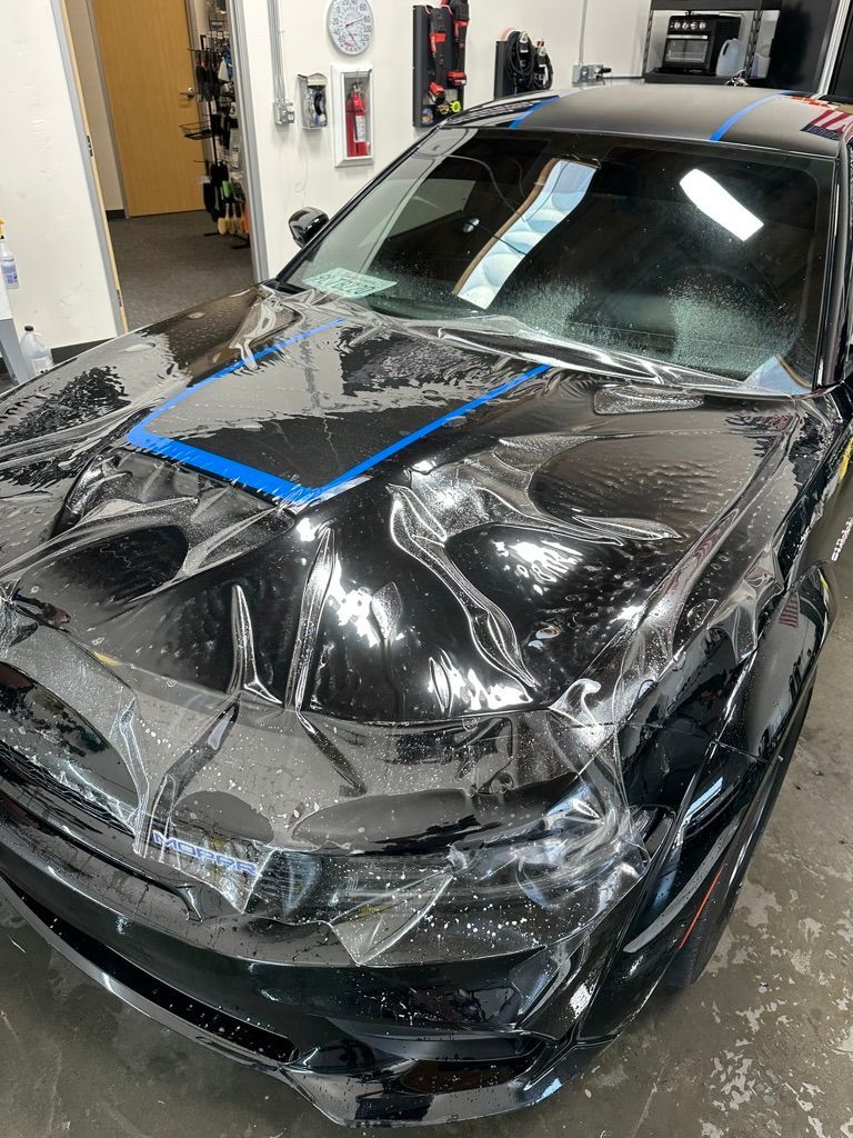 Black car hood covered in clear protective film during application process.