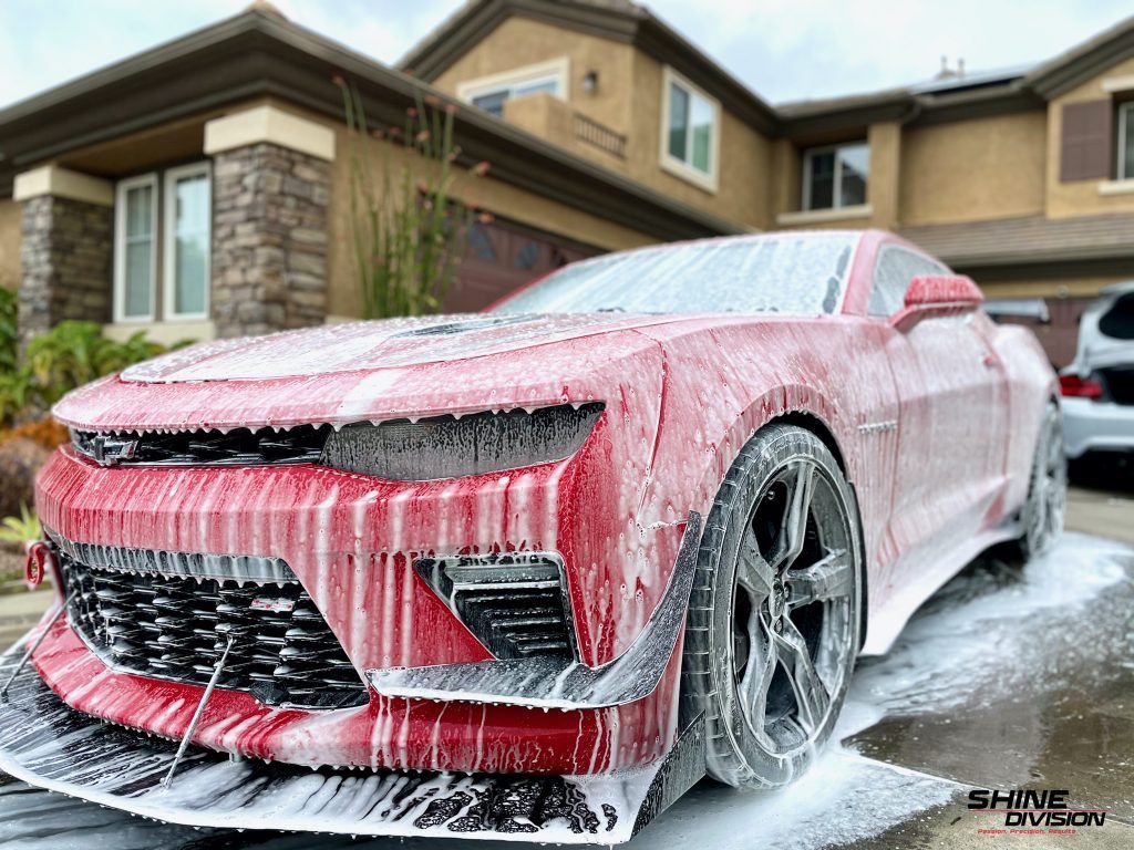 A red car is covered in foam in front of a house.