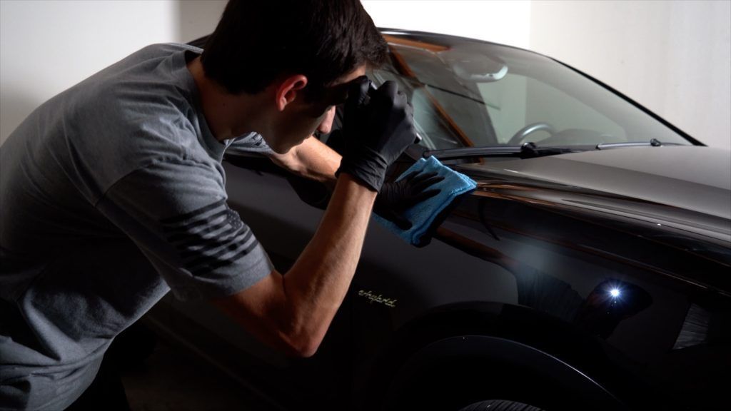 A man is cleaning a car with a cloth in a garage.