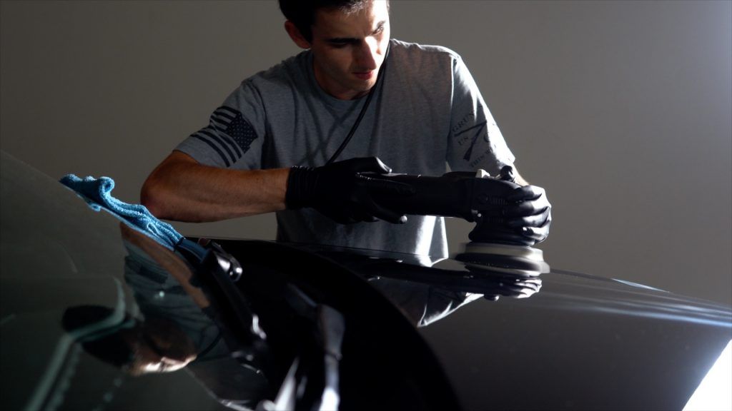 A man is polishing a car windshield with a machine.