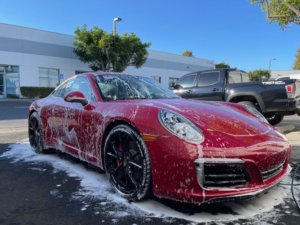 A red porsche 911 is covered in foam in a parking lot.