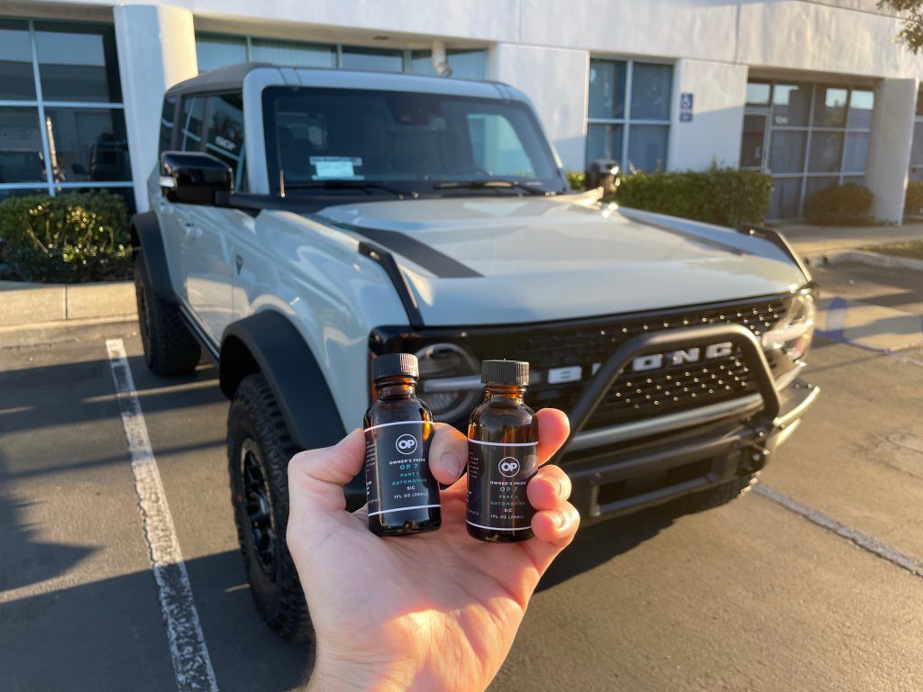 A person is holding two bottles in front of a ford bronco.