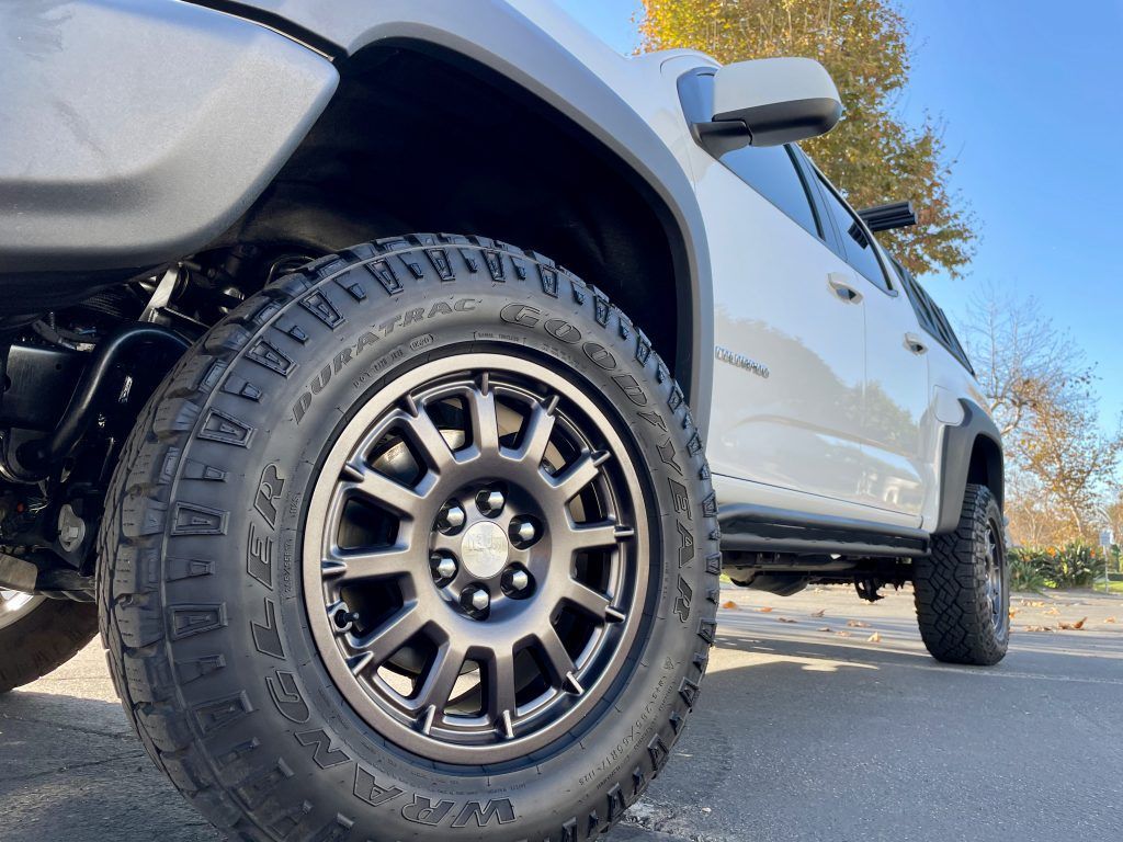 A white truck with black wheels and tires is parked on the side of the road.