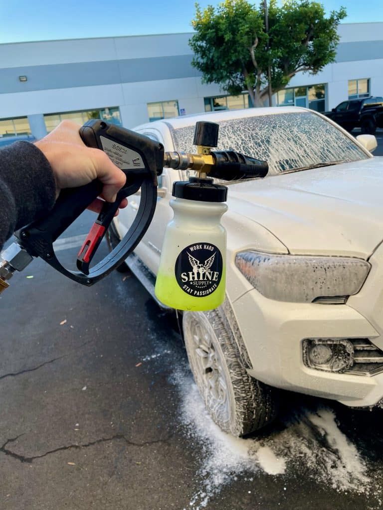 A person is washing a white truck with a spray bottle.