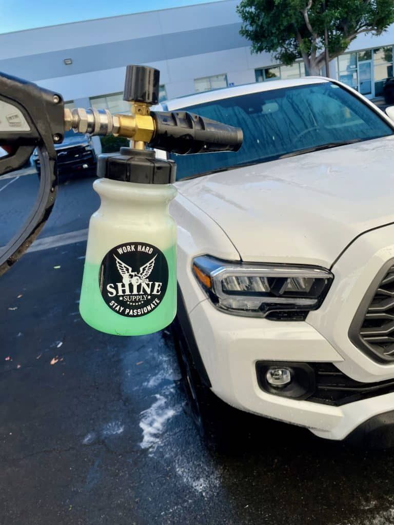 A person is washing a white truck with a spray bottle.