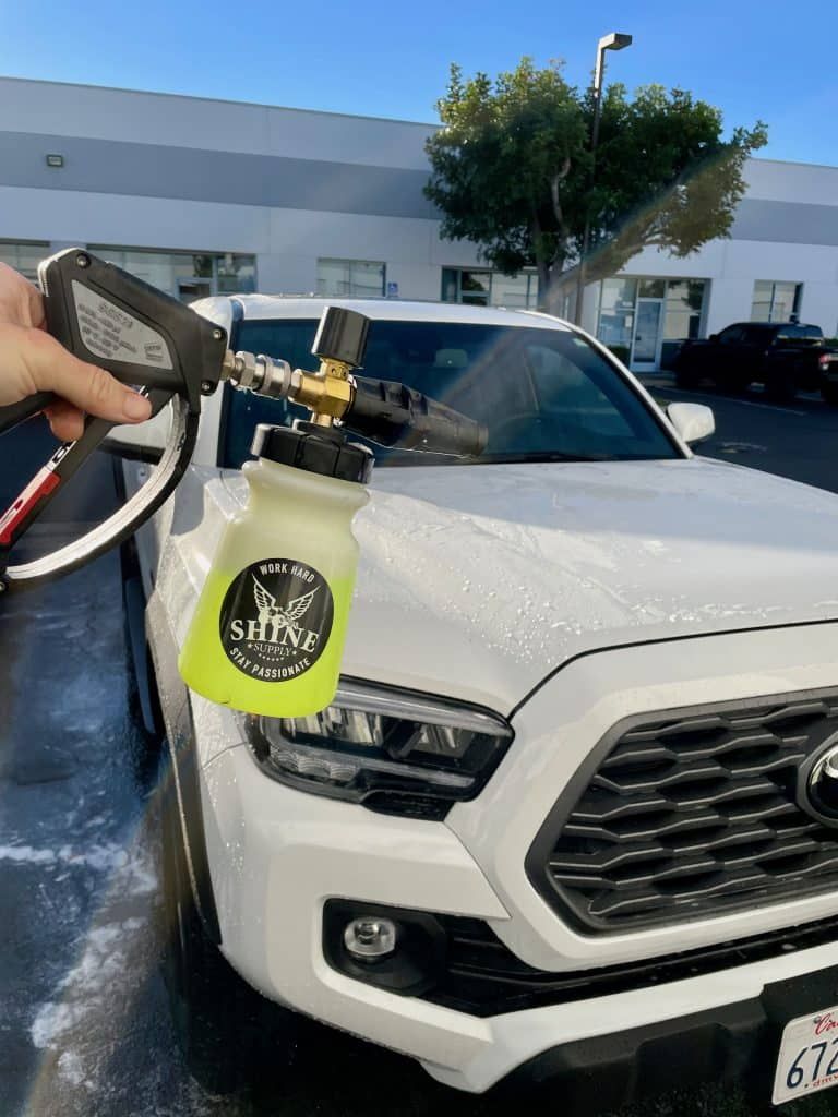 A person is washing a white truck with a spray bottle.
