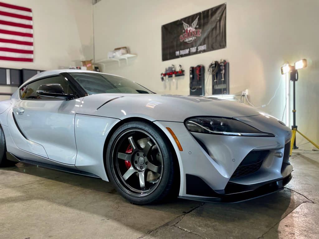 A white sports car is parked in a garage next to an american flag.