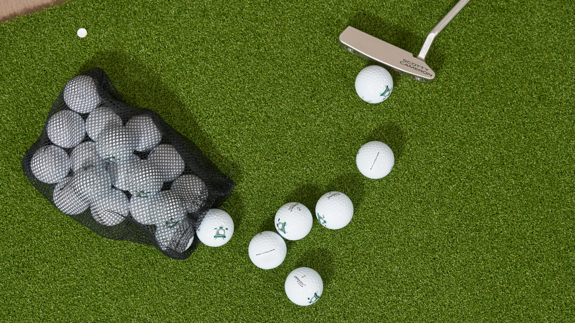 Golf balls scattered beside a ball basket and club on green turf