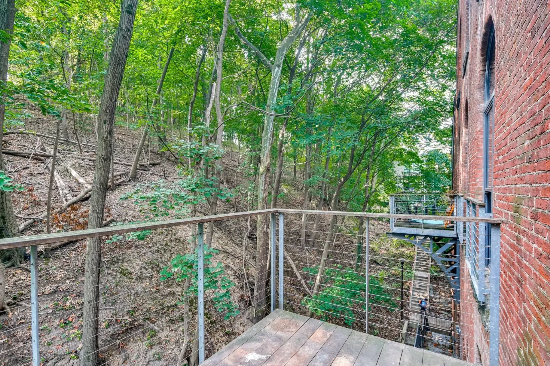 a wooden deck with a metal railing is surrounded by trees and a brick building .