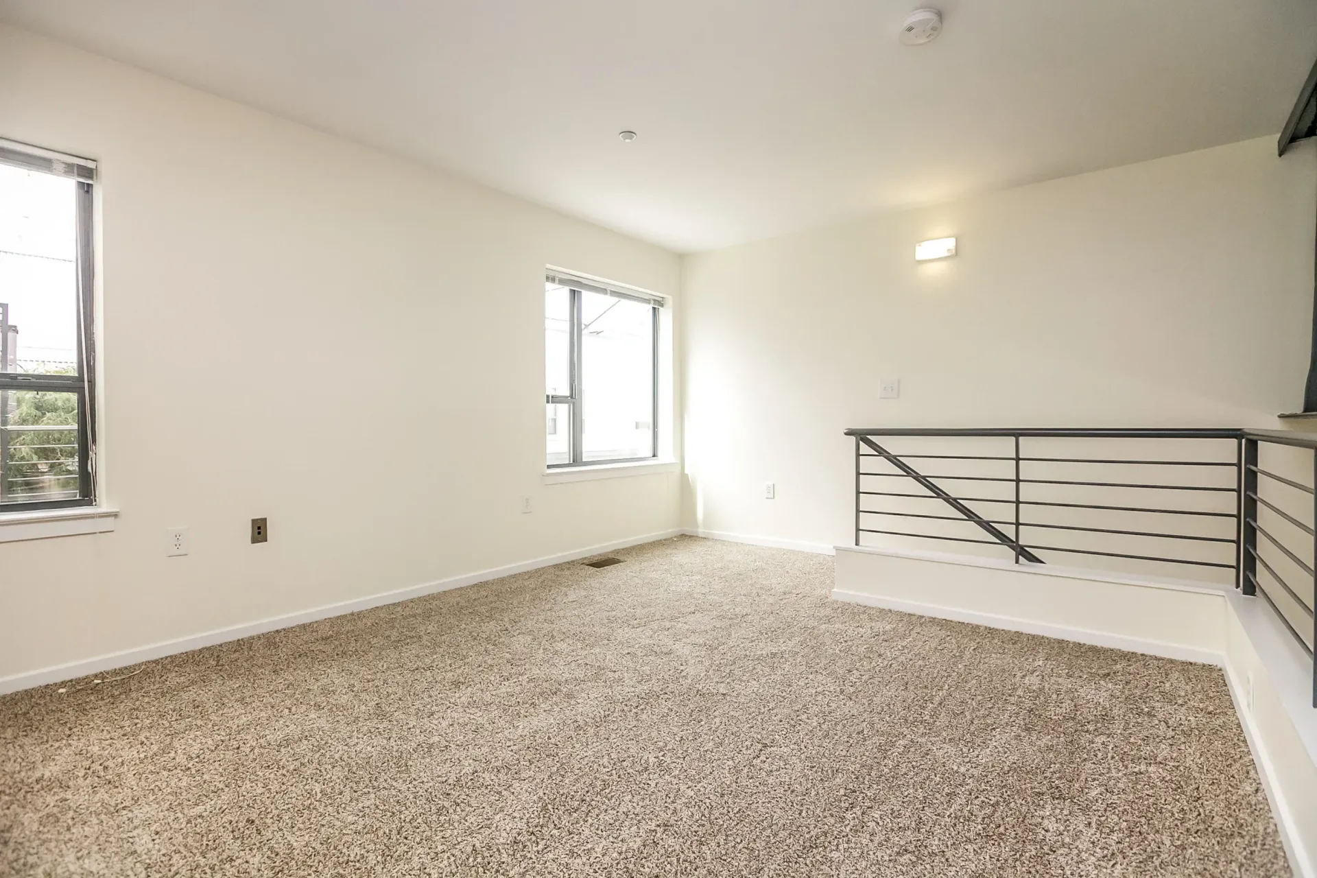 an empty room with a carpeted floor and two windows .
