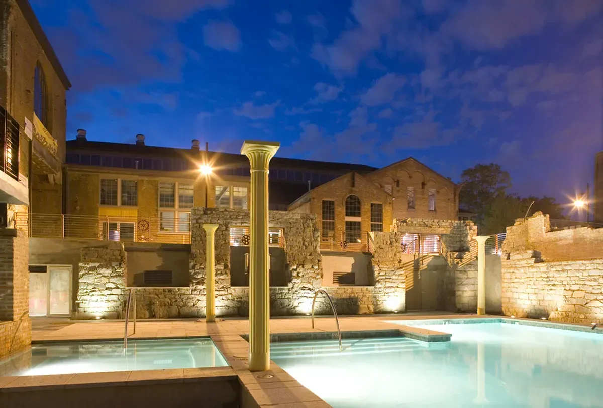 a large swimming pool is lit up at night in front of a building