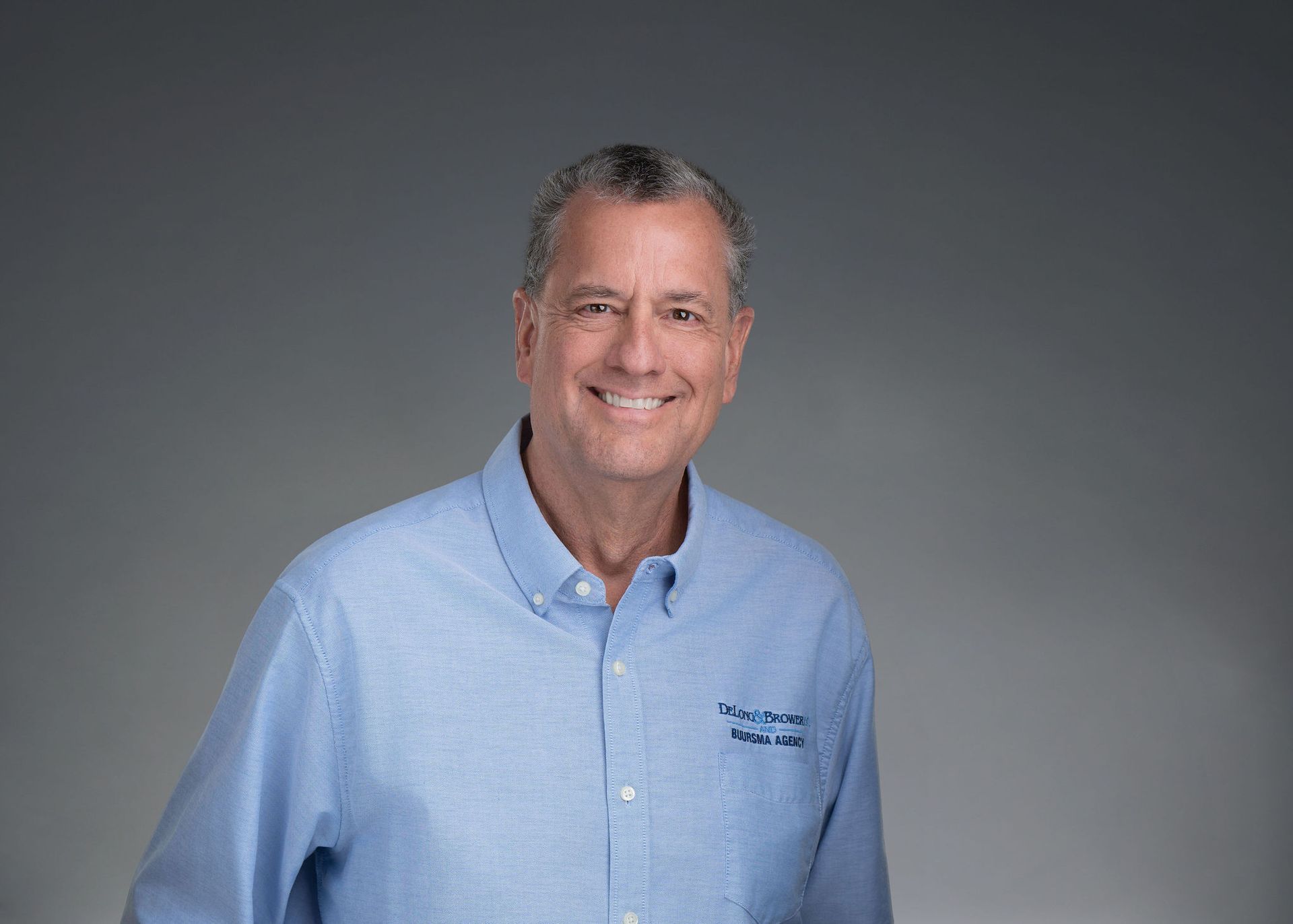 Smiling man in a light blue shirt against a gray background