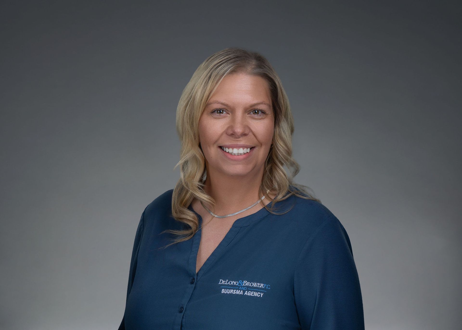 Portrait of a smiling blonde woman in a blue blouse against a gray background