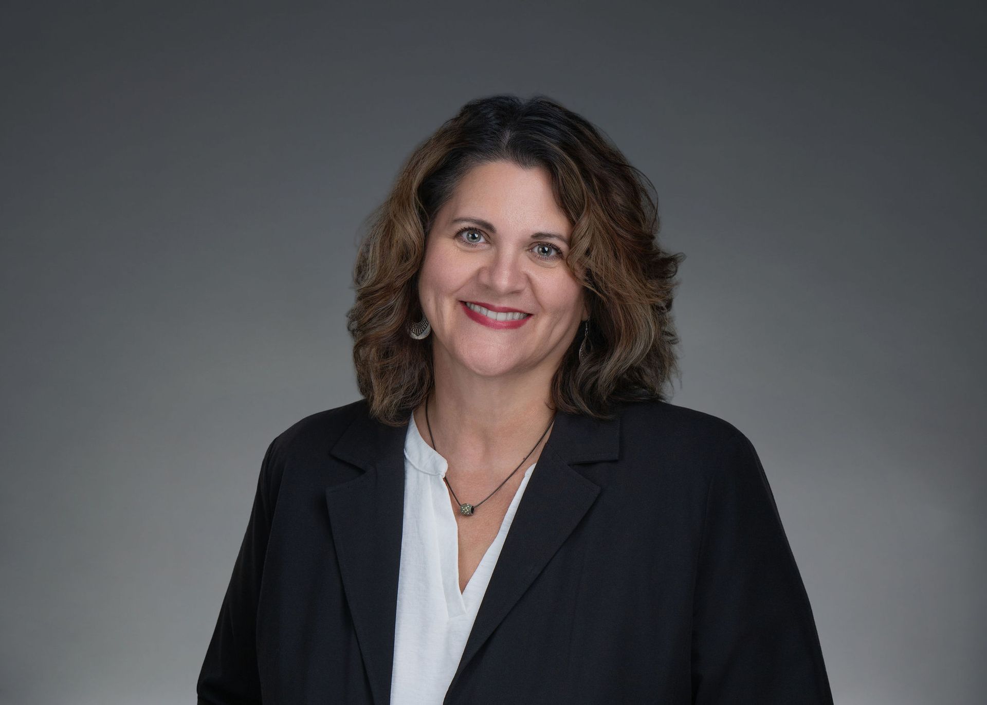 Smiling woman in black blazer and white blouse against a gray background