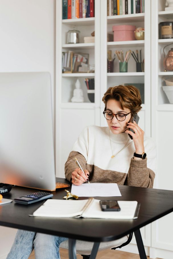 Person working at a desk, talking on phone and writing notes in a bright home office