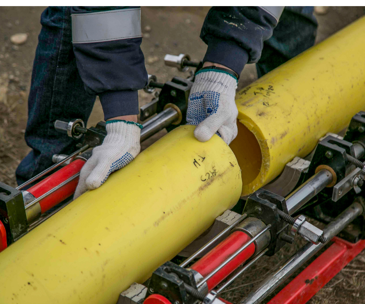 A worker joining two yellow pipes with their hands, using clamps, outdoors.
