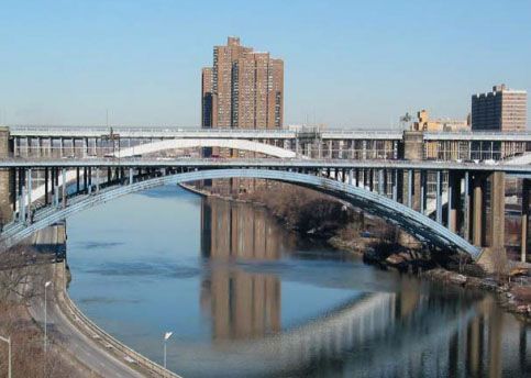 Blue arch bridge over water, apartment buildings in the background under a clear sky.