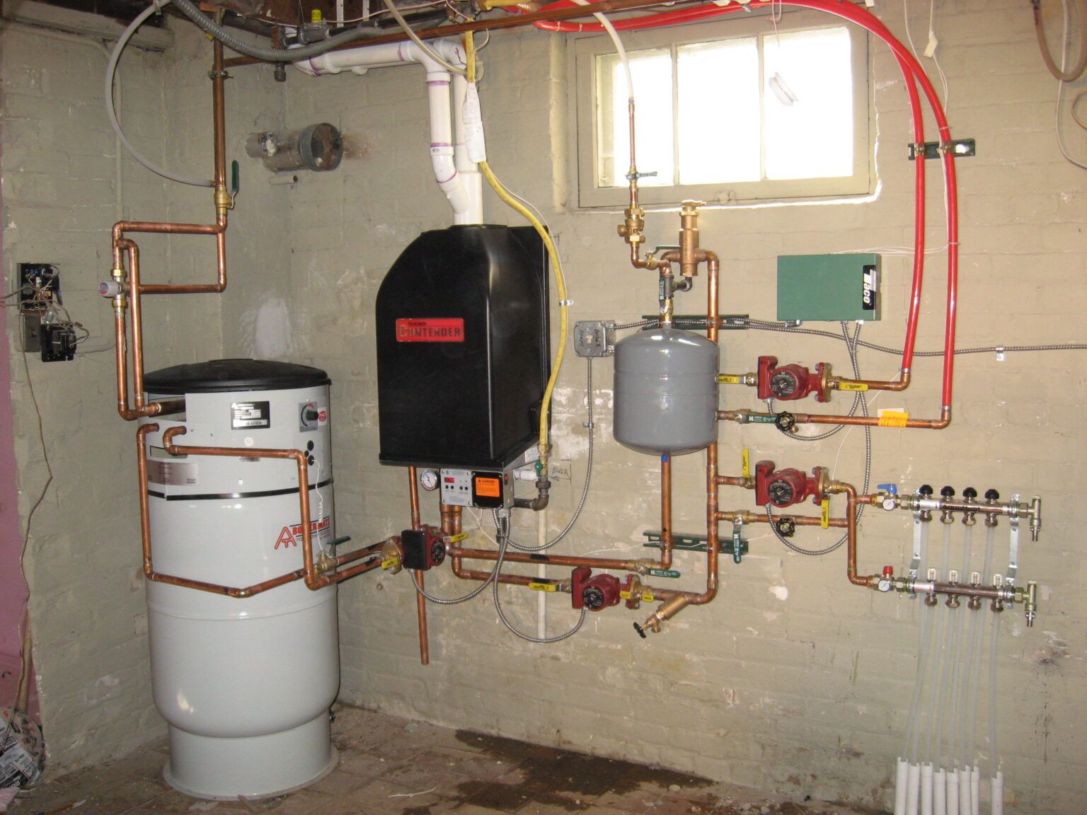 Complex residential hydronic heating system with copper pipes, boiler, and pumps against a concrete wall.