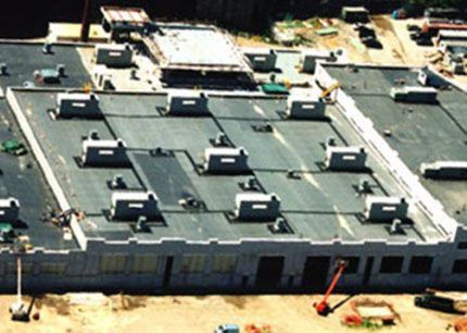 Aerial view of a commercial building under construction with numerous rooftop HVAC units and a flat roof.