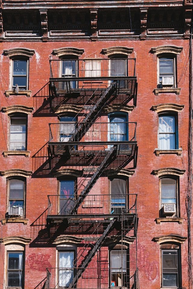 Red brick building with a black fire escape, windows, and air conditioners.
