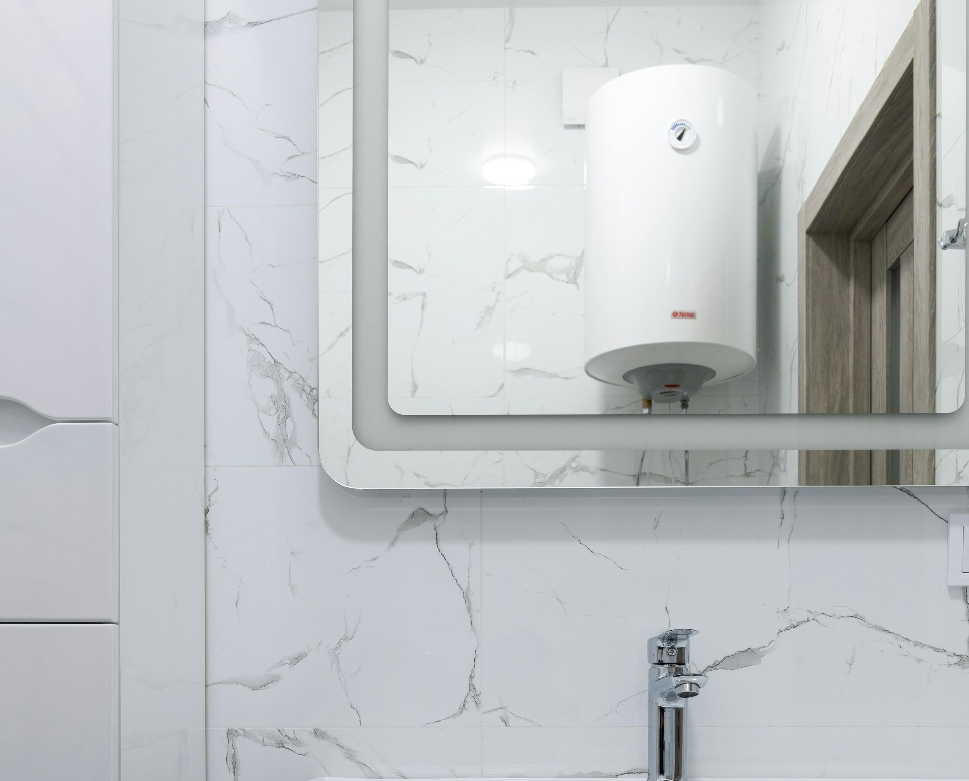Bathroom with white marble tile, illuminated mirror, and water heater.
