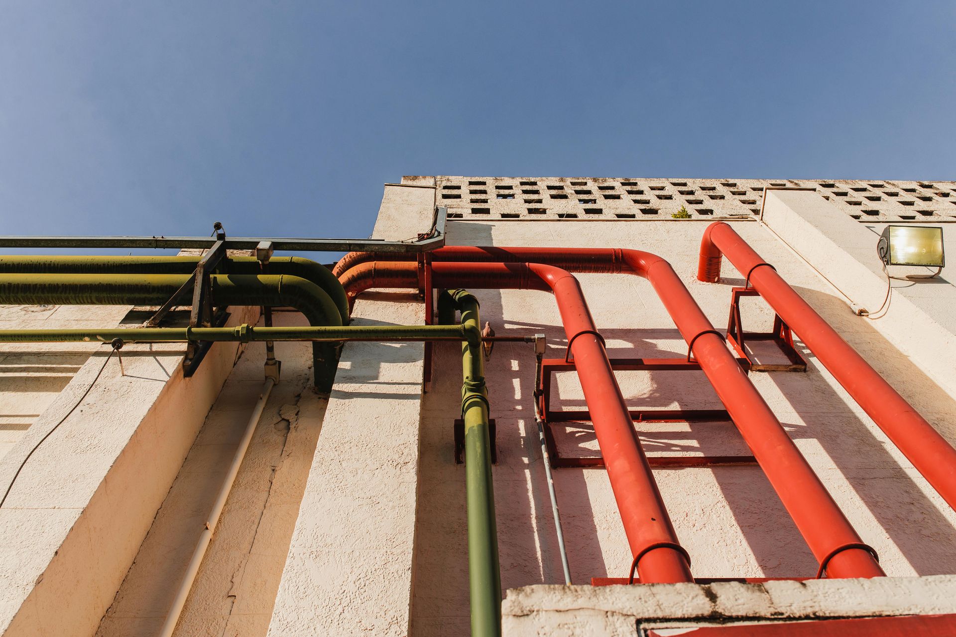 Red and green pipes running along a building wall against a blue sky