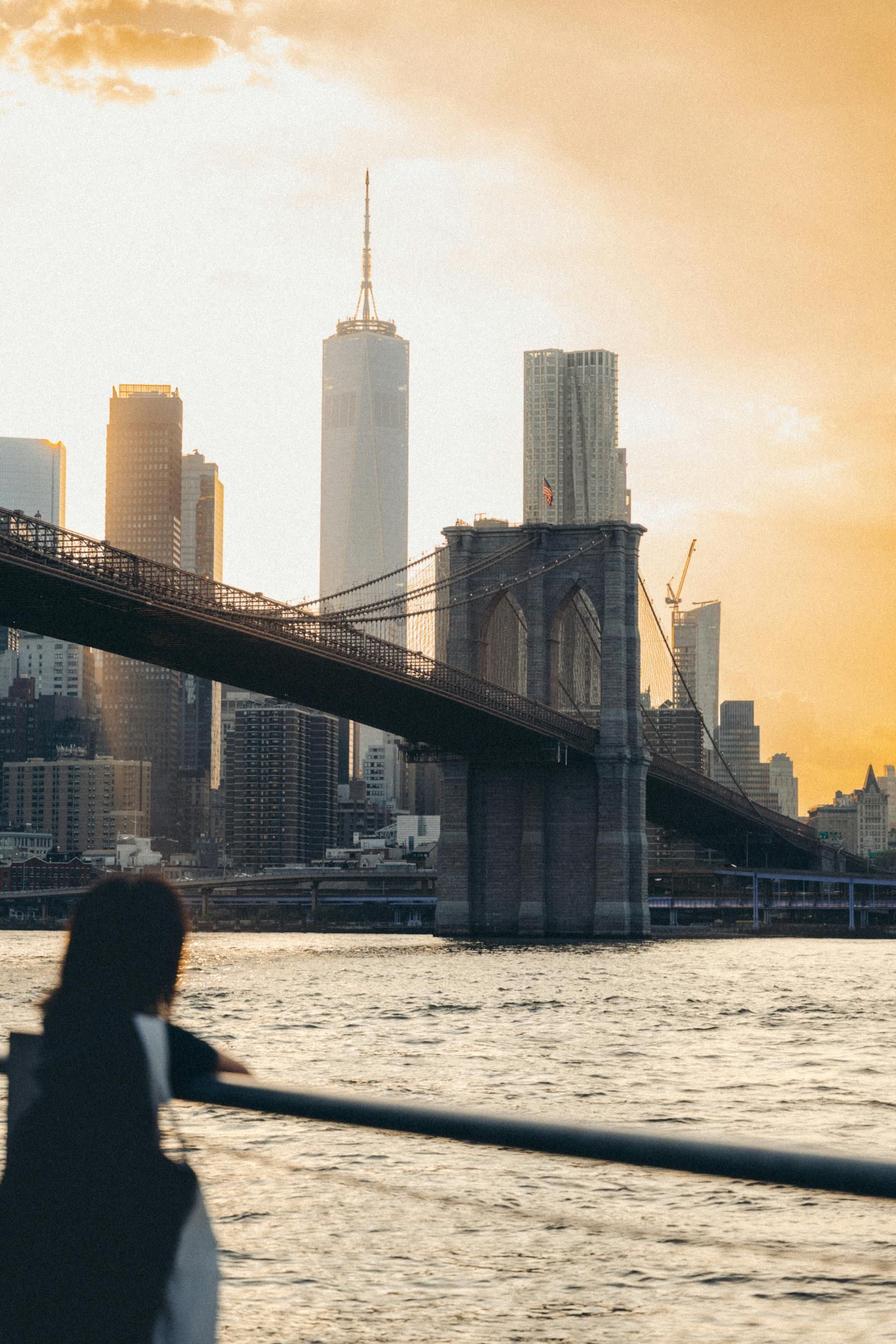 Woman overlooking Brooklyn Bridge and NYC skyline at sunset.