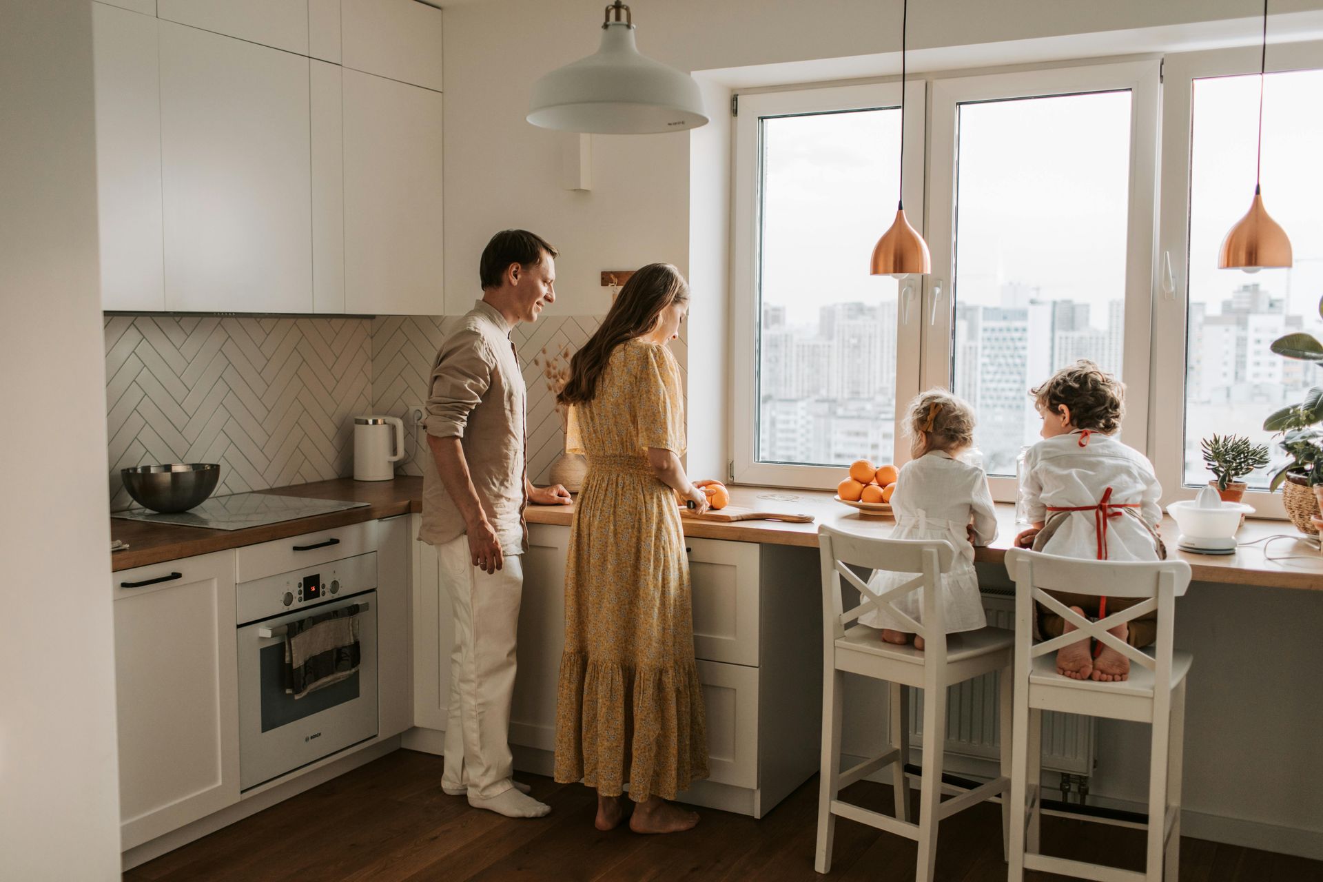 Woman in red cardigan slices tomatoes, child watches at a table in the kitchen.