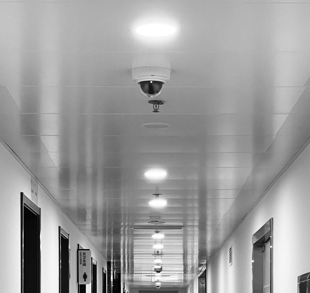 Long hallway with ceiling lights, doors on each side, and a security camera.
