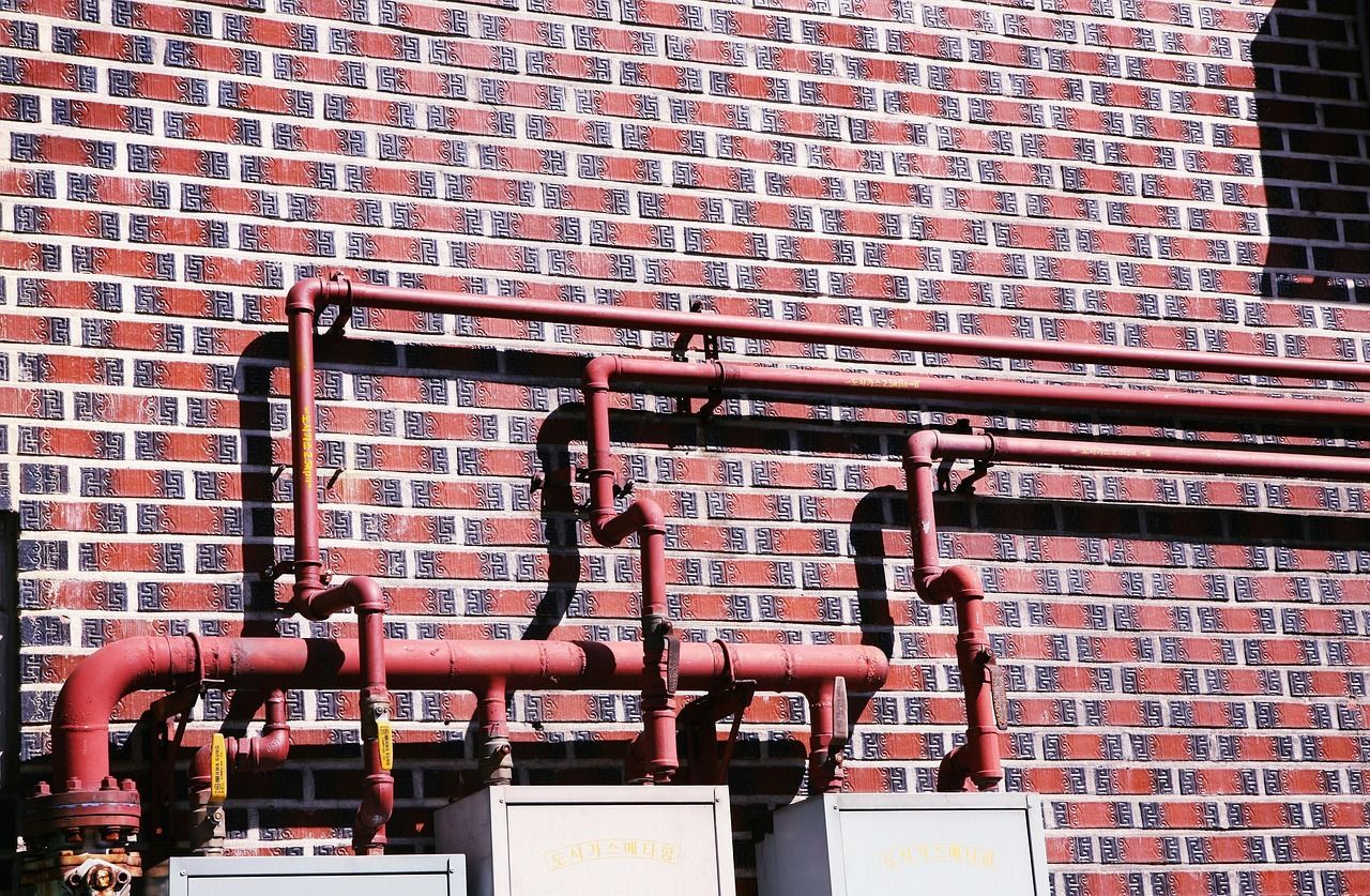 Red pipes on brick wall, sunlit, possibly industrial.