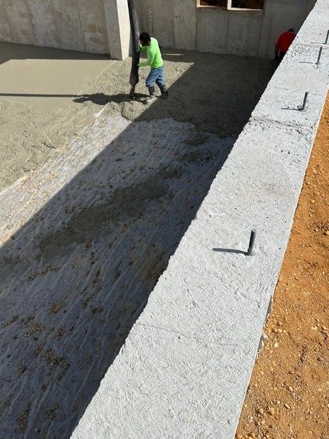 A man in a green shirt is pouring concrete into a concrete wall