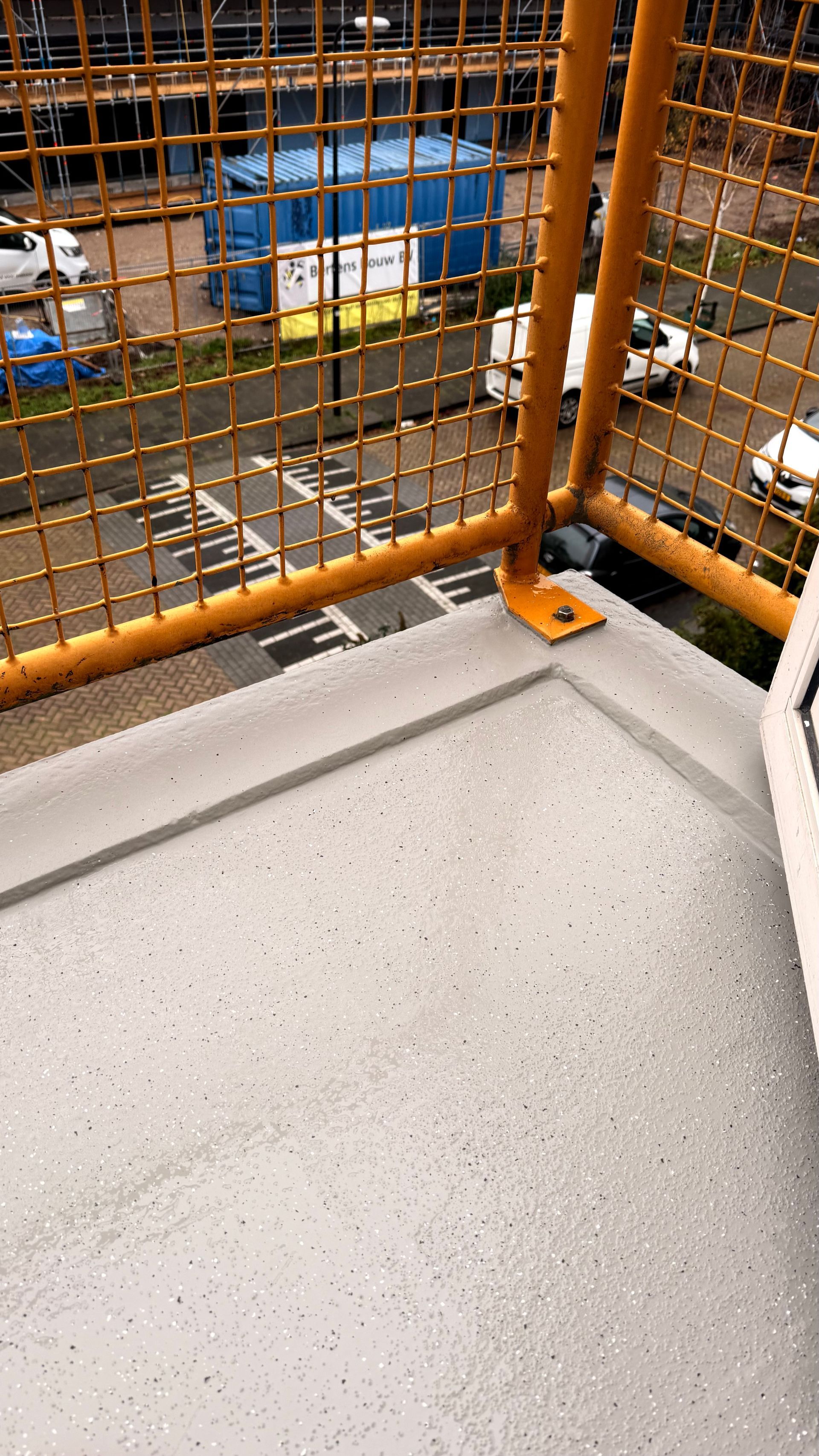 Uitzicht vanaf een hoge, geel omheinde richel met uitzicht op een straat en een bouwterrein.