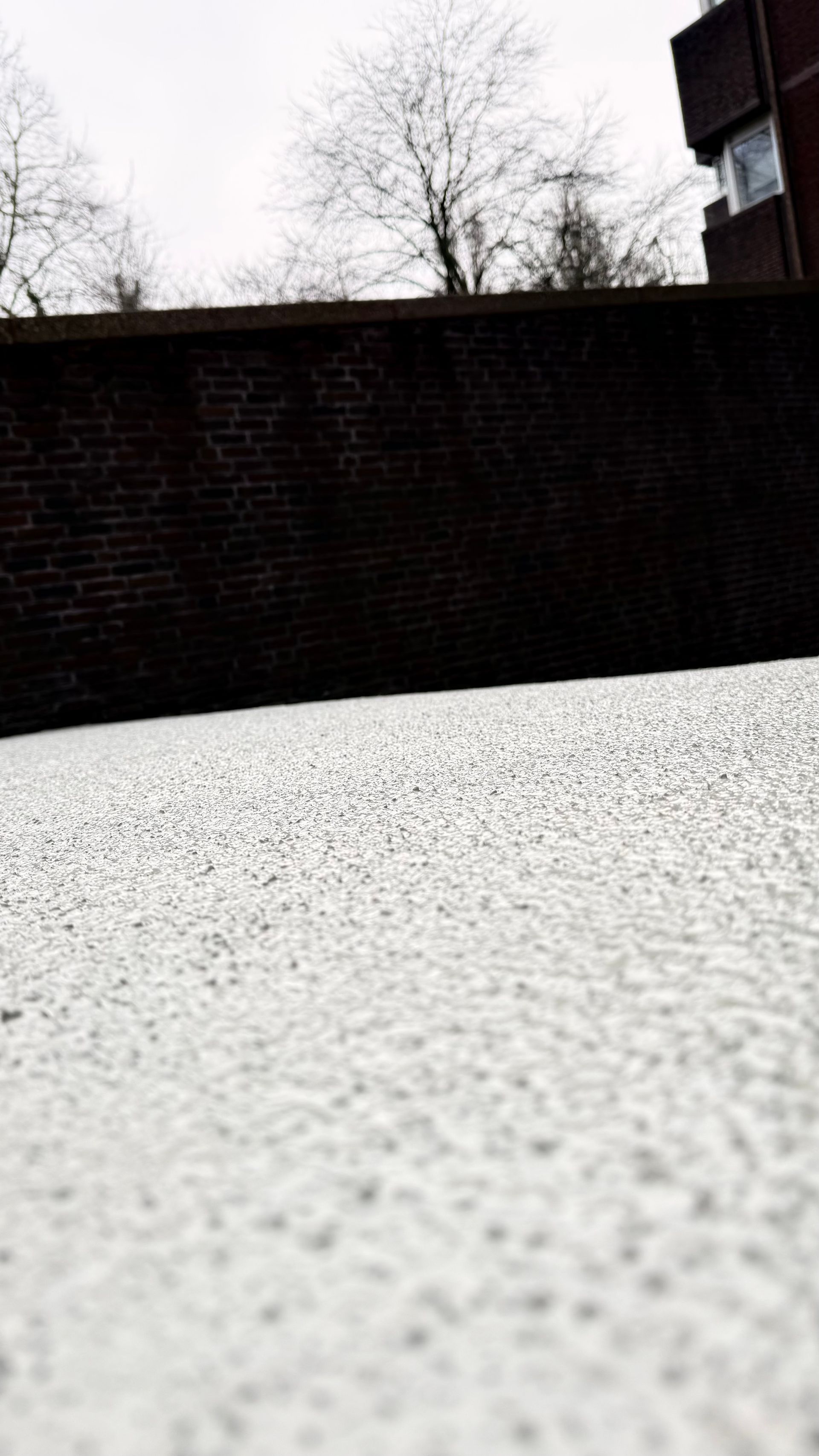 Een bakstenen muur tegen een bewolkte hemel. Op de voorgrond is een wit, gestructureerd oppervlak te zien.