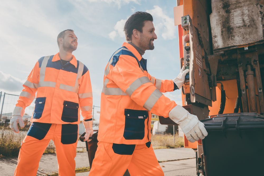 Two Waste Collection Workers in Orange Safety Gear Loading a Trash Bin Into a Truck — Red E Bins In Wauchope, NSW