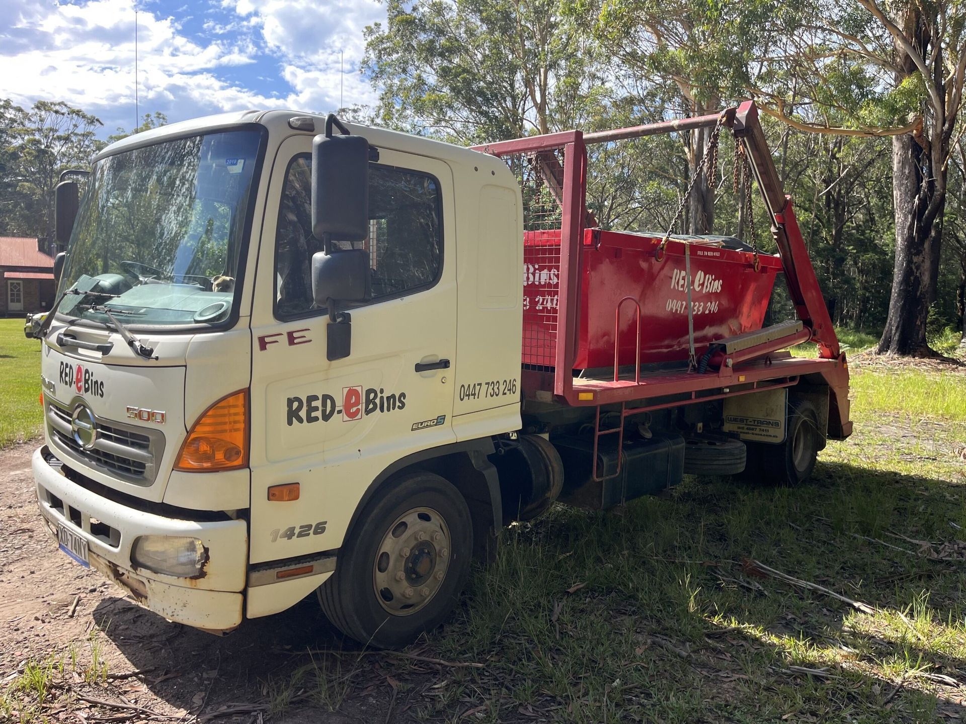 A white truck with a red bin on the back is parked in a grassy area.  — Red E Bins In Lake Cathie, NSW