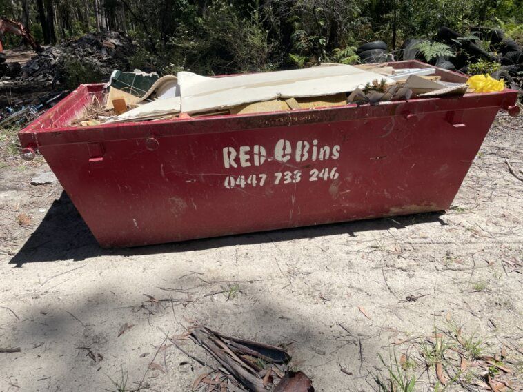 A red skip bin filled with rubbish sitting in the dirt — Red E Bins In Lake Cathie, NSW