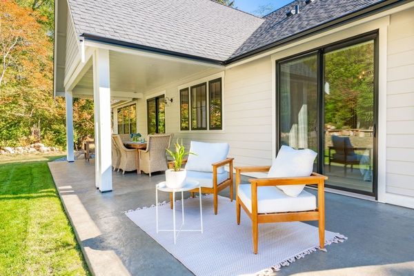 A patio with chairs and a table in front of a white house.