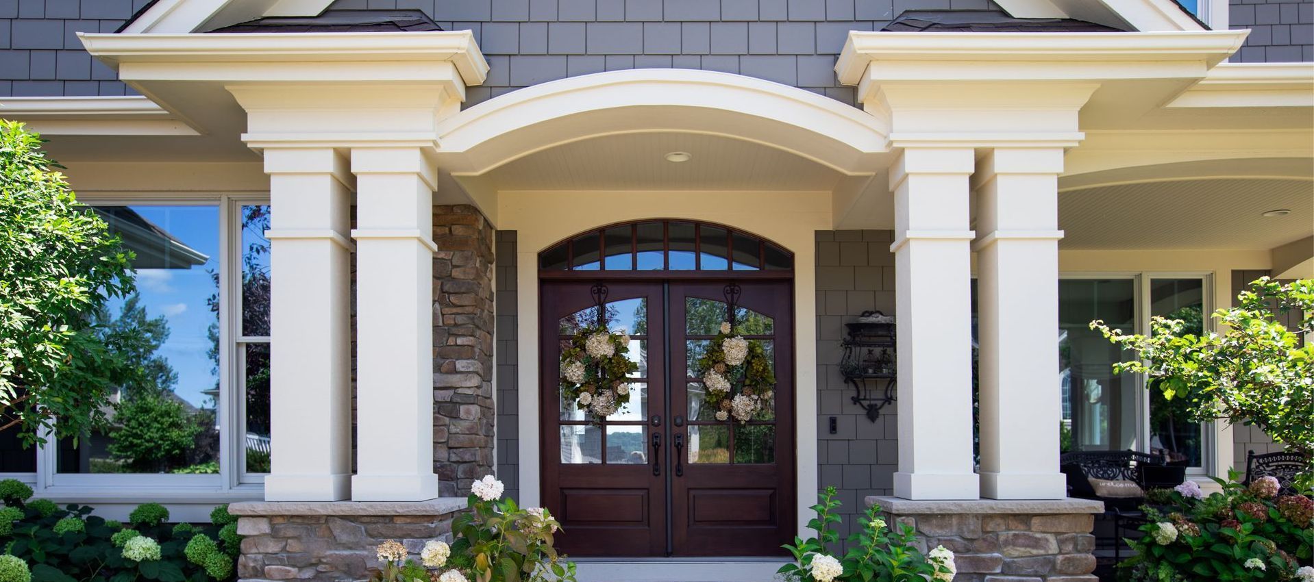 The front door of a house with a porch and flowers in front of it.